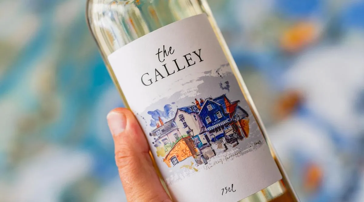 A bottle of The Galley white wine, its watercolour Topsham label held to the light