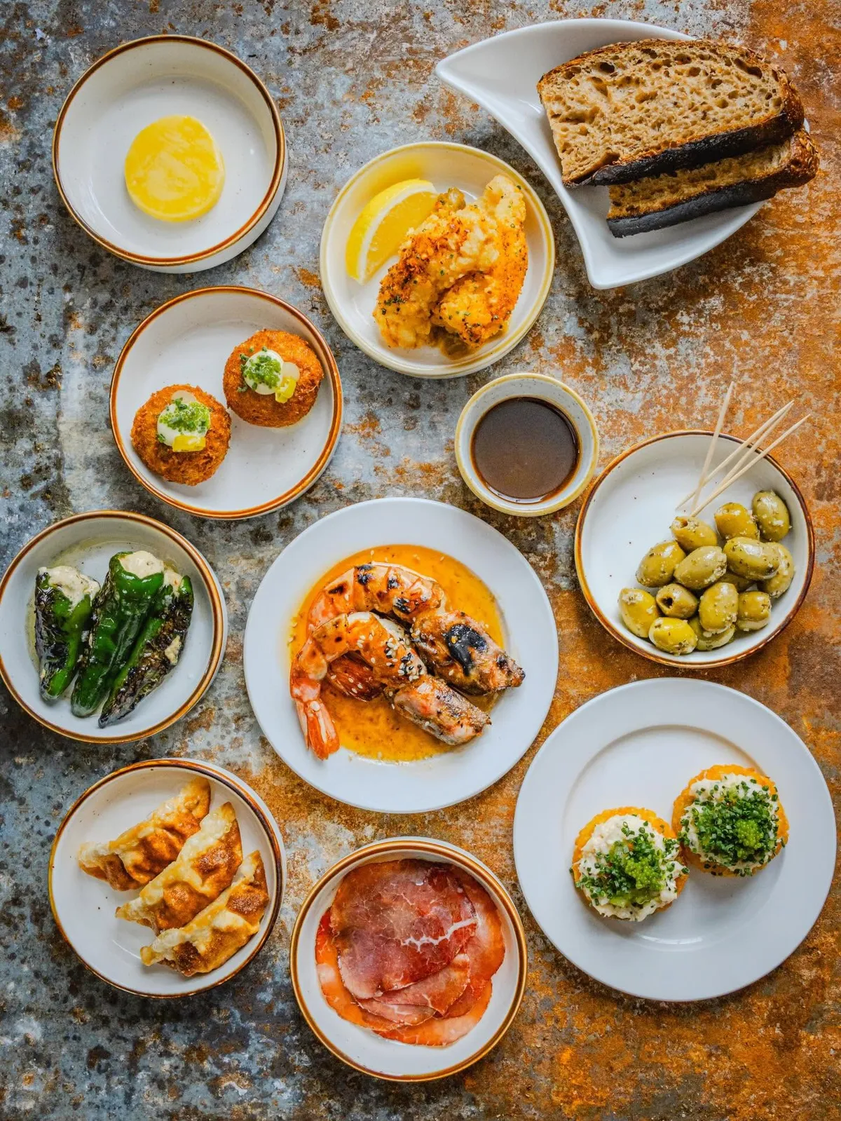 A spread of small plates — sourdough, marinated olives, croquettes, grilled king prawns, gyoza and charcuterie